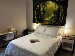 Hotelkamer met een bed, bureau, stoel, nachtkastje en een wanddecoratie van een boslandschap.