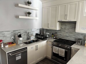 A modern kitchen with white cabinets, a stainless steel dishwasher, a built-in oven, and a coffee maker. - Fox - Private Bedroom near Downtown and 17th Av (Calgary)