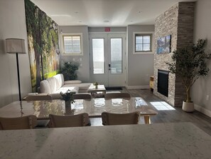 A modern living room with a sofa, a dining table with chairs, a fireplace, and a large painting on the wall. - Fox - Private Bedroom near Downtown and 17th Av (Calgary)