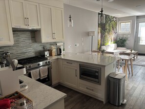 A modern kitchen with a central island, built-in appliances, and a dining area with a view of the outdoors. - Fox - Private Bedroom near Downtown and 17th Av (Calgary)