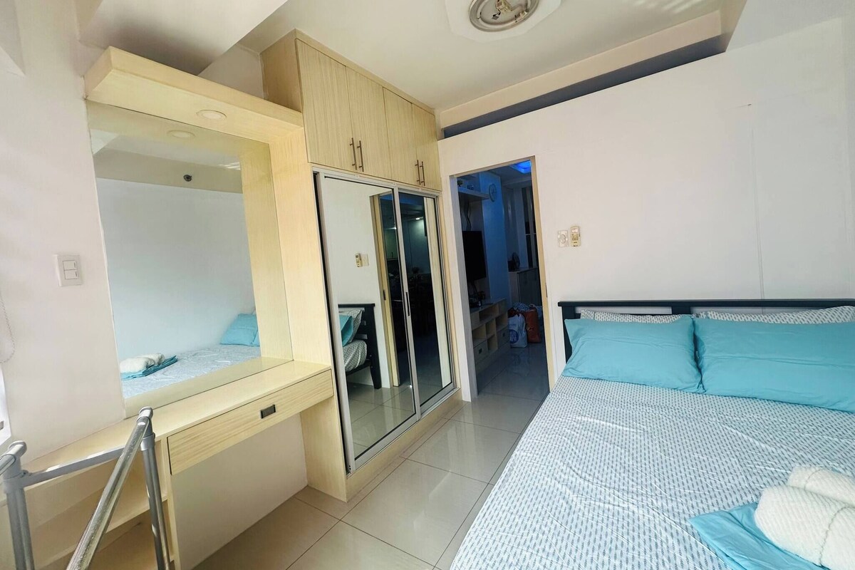 Um quarto com uma cama, um guarda-roupa, um espelho e uma porta que dá para outro espaço.