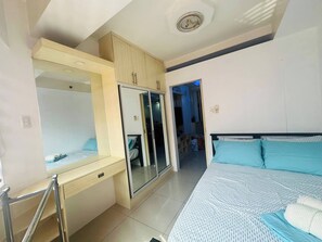 Ein Schlafzimmer mit einem Bett, einem Kleiderschrank, einem Spiegel und einer Tür zu einem anderen Raum.