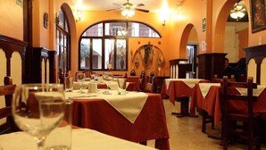 Comedor con mesas dispuestas para una comida, ventilador de techo y un ventanal con luz natural.