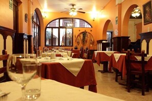 Comedor con mesas dispuestas para una comida, ventilador de techo y un ventanal con luz natural.
