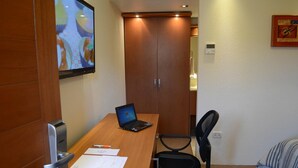 Habitación de hotel con escritorio de madera, una computadora portátil, documentos, una silla y una cama con manta a rayas.