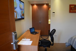 Habitación de hotel con escritorio de madera, una computadora portátil, documentos, una silla y una cama con manta a rayas.