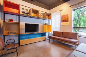 Ein modernes Wohnzimmer mit Flachbildfernseher, Einbauschränken, einem braunen Ledersofa und einem Fenster mit Blick auf Bäume.