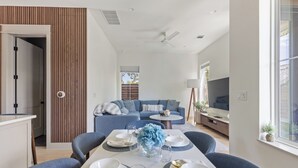 A modern living room with a sofa, TV, and dining area with chairs and a table set for two. - Beautiful 4-bedroom - Pool, Patio, Grill - Close to UT & Rainey (Austin)