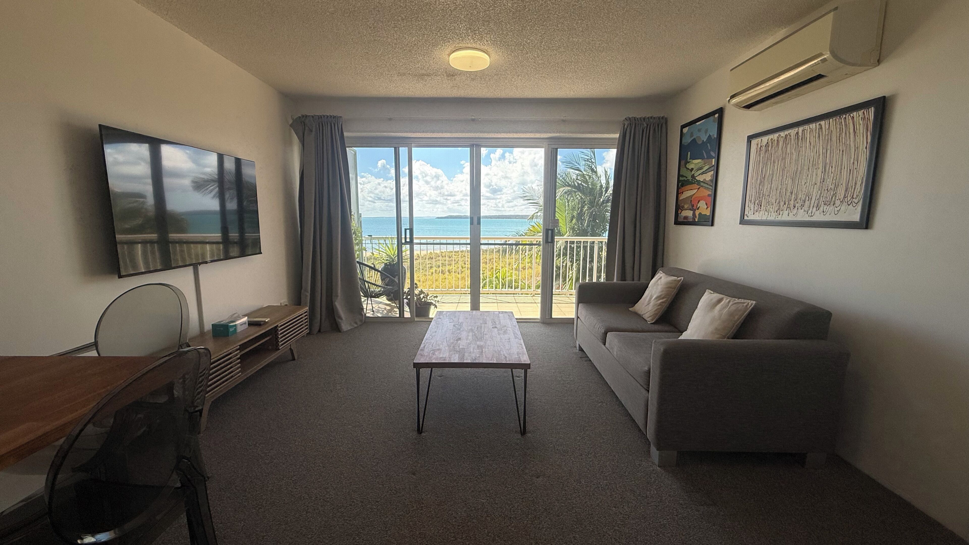 A furnished room with a sofa, a table, a TV, and a balcony with a view.