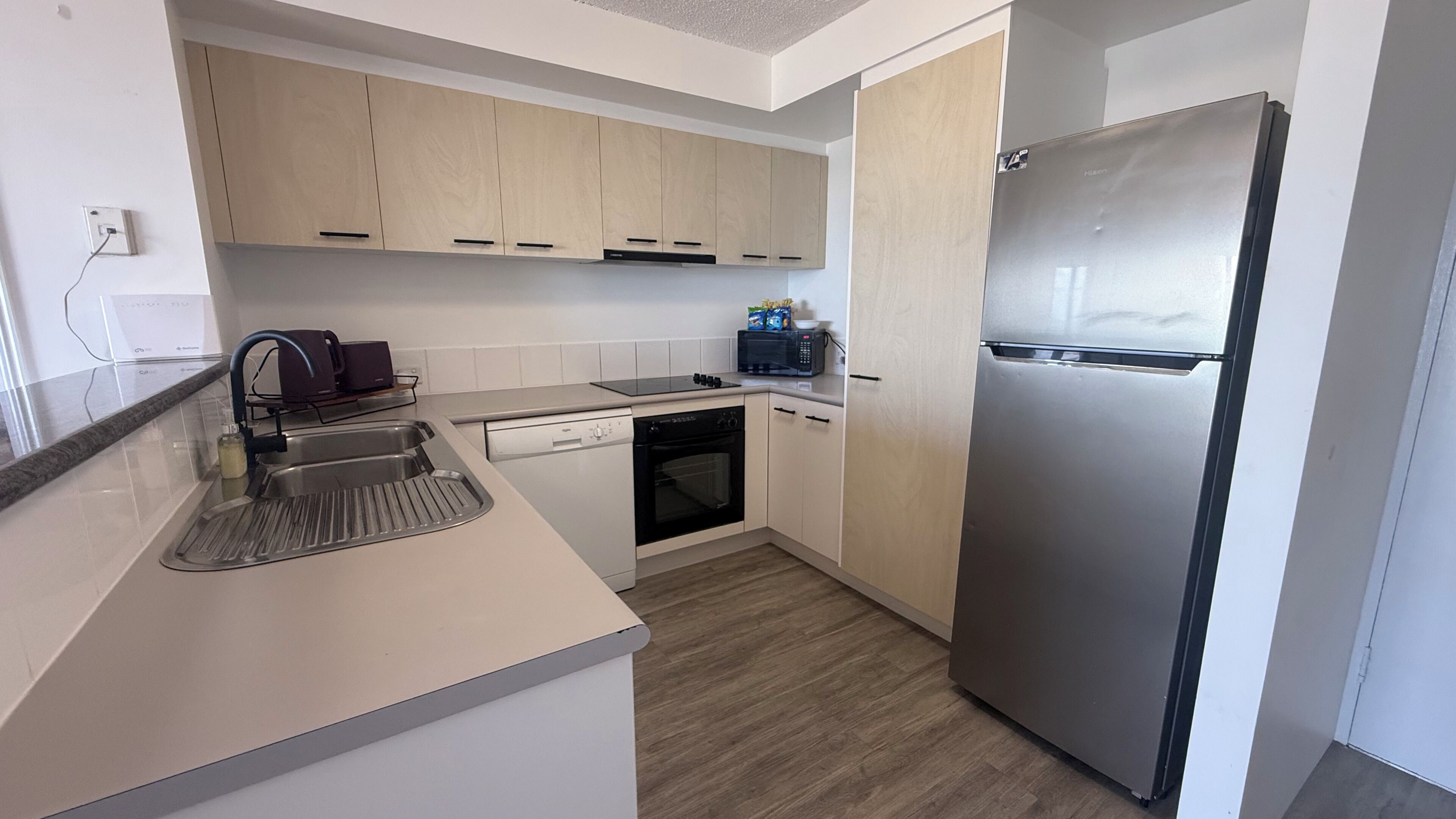 A modern kitchen with light wood cabinets, a stainless steel refrigerator, a built-in oven, and a dishwasher.