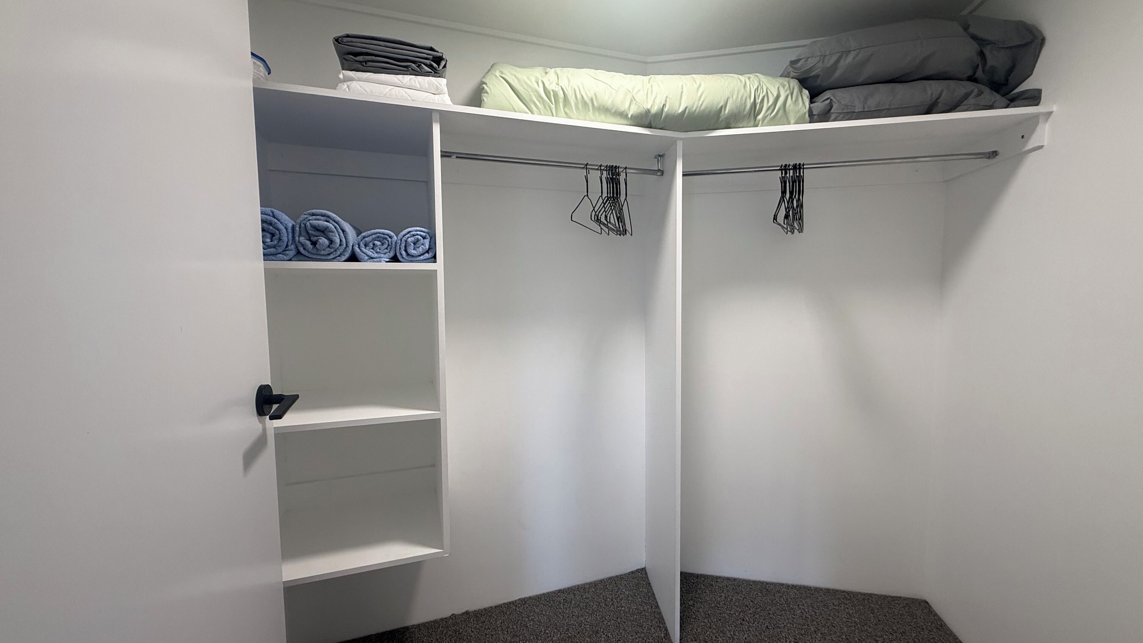 A walk-in closet with a bed on top, shelves with folded clothes, and a hanging rod.