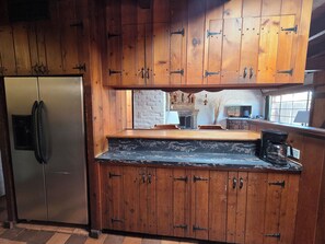 A kitchen with wooden cabinets, a marble countertop, a stainless steel refrigerator, and a brick fireplace. - Unique 2-bedroom Castle house near U of A (Tucson)