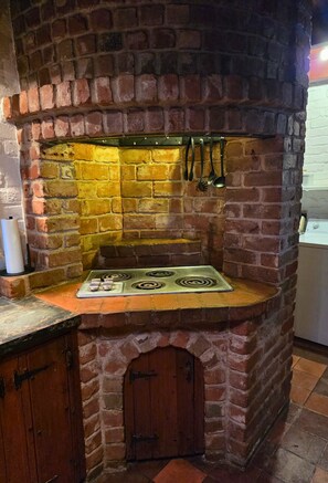 A brick kitchen with a built-in stove, hanging utensils, and a wooden door.