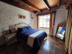 A bedroom with a bed, a nightstand, a window, and a mirror.