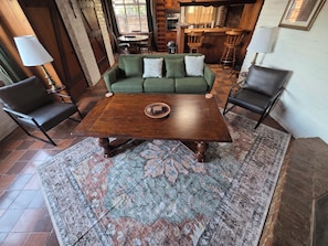 A cozy living area with a green sofa, two wooden chairs, a dark wooden coffee table, and a patterned rug.
