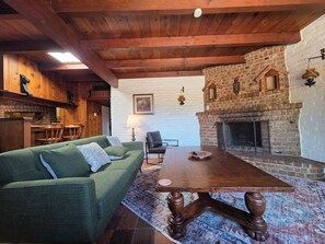 Un salon chaleureux avec un canapé vert, une table basse en bois et une cheminée en briques.