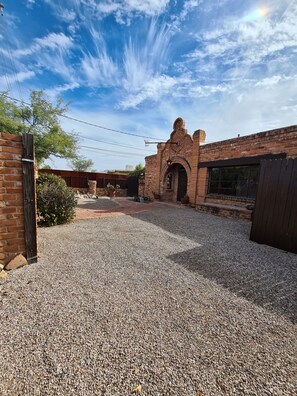 A courtyard with a gravel ground, a brick building with an arched entrance, and a wooden fence. - Unique 2-bedroom Castle house near U of A (Tucson)