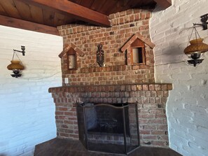 A brick fireplace with a glass door, wooden beams, and two wall-mounted lanterns.