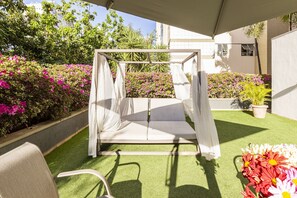 Ein Garten mit einer weißen Sitzgelegenheit im Freien, darunter ein Schaukelsessel und ein Tisch.