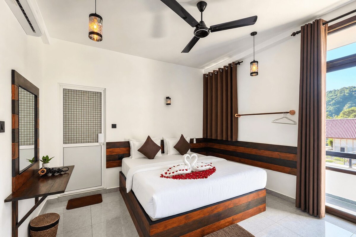 A hotel room with a bed, a desk, a ceiling fan, and a view of the outdoors.