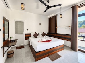 A hotel room with a bed, a desk, a ceiling fan, and a view of the outdoors.