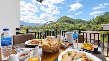 A breakfast table with various food items, a water bottle, and a view of a mountainous landscape.