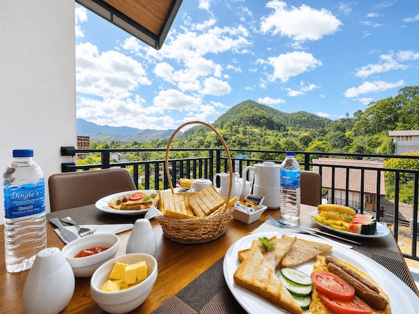 A breakfast table with various food items, a water bottle, and a view of a mountainous landscape.