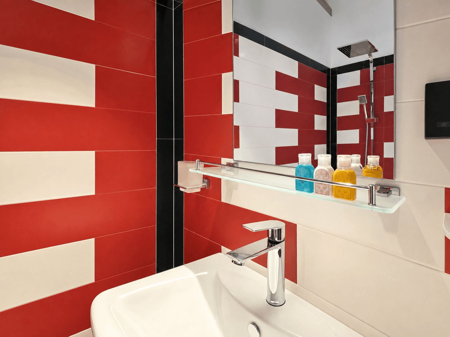 A modern bathroom with a white sink, chrome faucet, and a glass shelf holding toiletries.