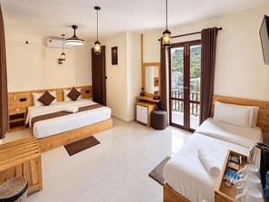 A hotel room with two beds, a desk, a small kitchenette, and a balcony with curtains.