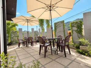 An outdoor patio with a table and chairs, surrounded by plants and a view of the city.