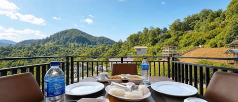 A dining table set with plates, bowls, and a water bottle on a balcony with a mountain view.