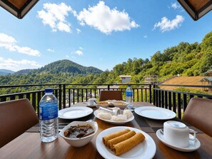 A dining table set with plates, bowls, and a water bottle on a balcony with a mountain view.