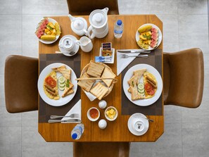 A dining table with breakfast items, including toast, eggs, and fruit, and a teapot.