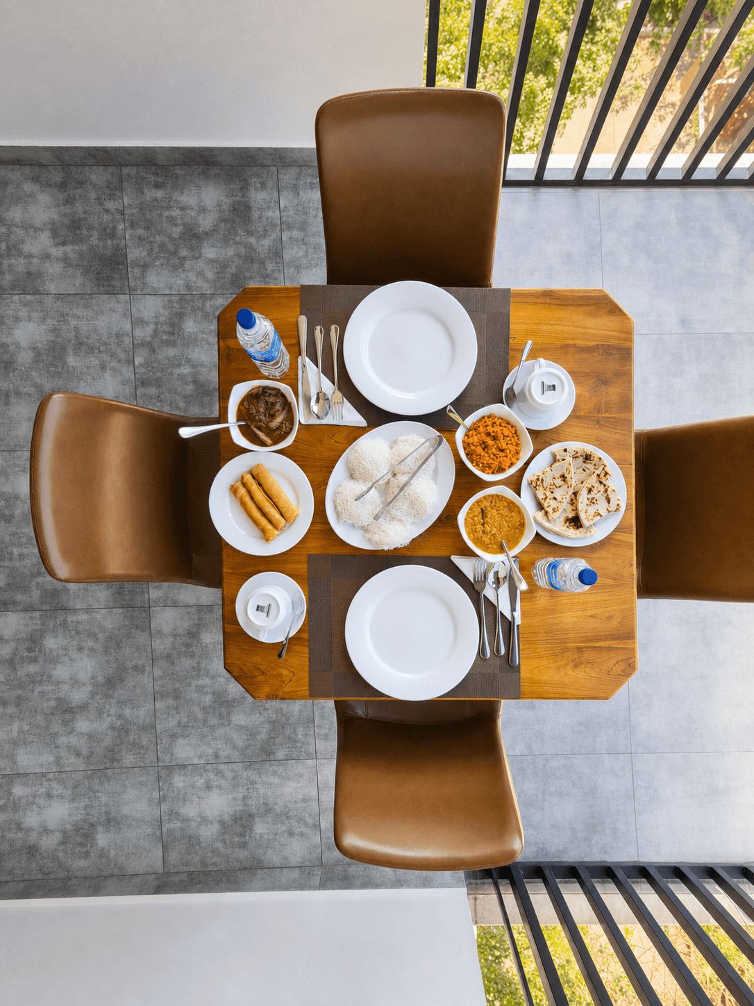 A dining table with a variety of dishes, including rice, flatbreads, and a bowl of curry, set for four people.