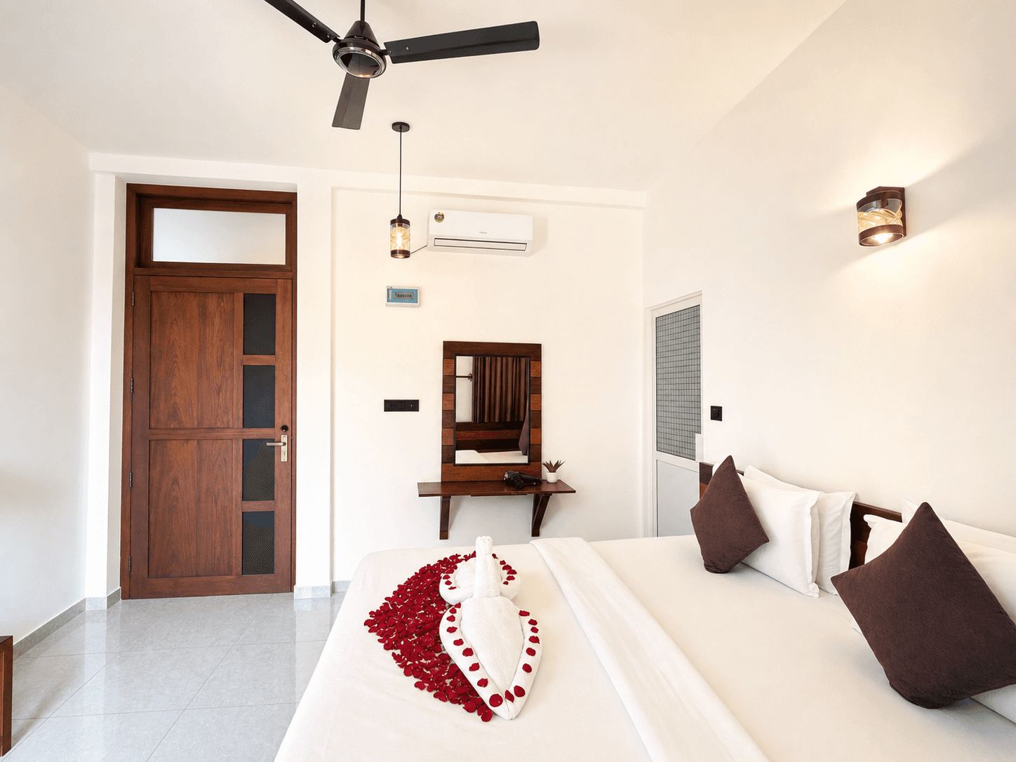 A hotel room with a bed, a desk, a mirror, a ceiling fan, and an air conditioning unit.
