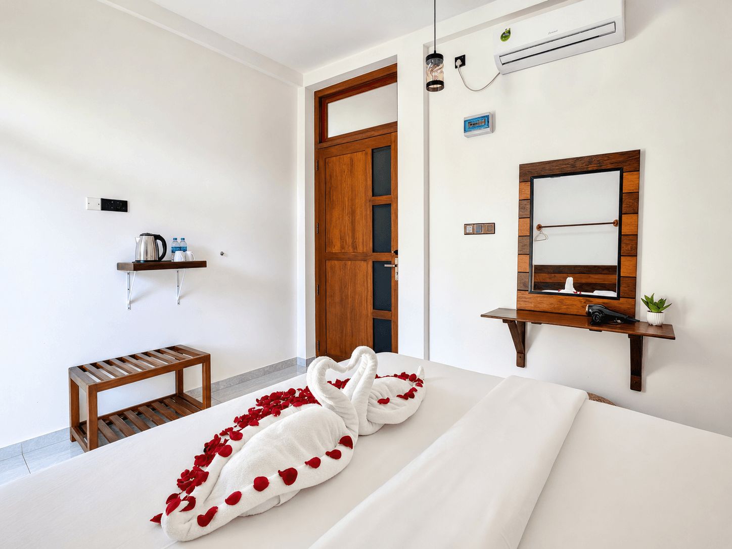Une chambre d’hôtel avec un lit, un banc en bois, un miroir et une étagère contenant des articles de toilette.