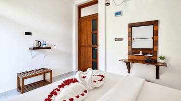 Une chambre d’hôtel avec un lit, un banc en bois, un miroir et une étagère contenant des articles de toilette.