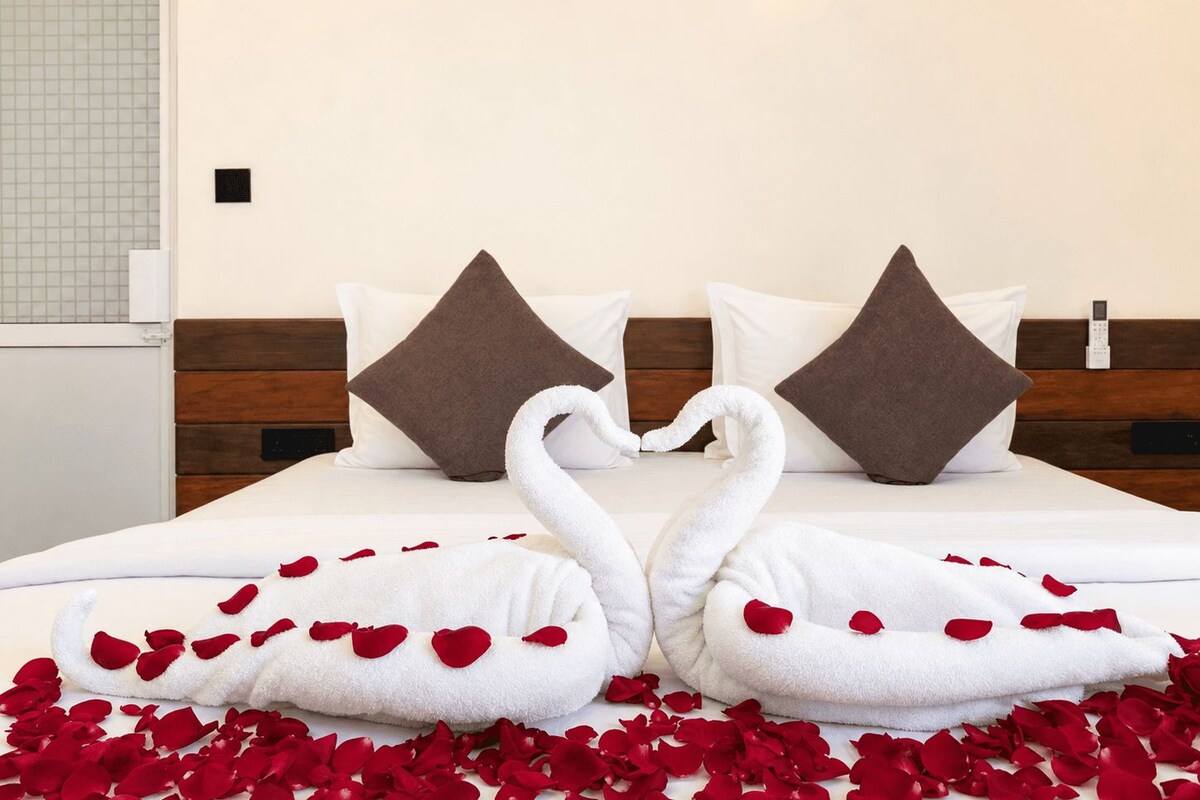 A hotel room with a bed, pillows, a bedside table, and a wall-mounted phone.