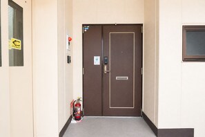 A hotel entrance with a brown door, a fire extinguisher, and a security panel. - SERENE | Nishikujo, 5th Floor | 100 ㎡, Sleeps 10 | Direct Access to USJ and Osaka Station (Konohana Ward)