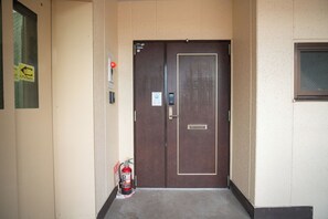 A brown door with a keypad lock, a fire extinguisher, and a small window to the right. - Aoba Residence ASAHI: 2-Minute Walk to Nishikujo Subway Station, 100 sqm, 4-Bedroom Residence Near USJ (大阪市)