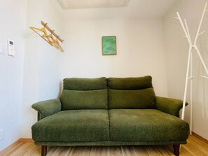 A green sofa in a room with a wooden floor, a wall-mounted heater, and a white wind turbine model. - SERENE | Nishikujo, 5th Floor | 100 ㎡, Sleeps 10 | Direct Access to USJ and Osaka Station (Konohana Ward)