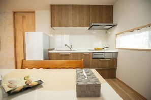 A compact kitchen with wooden cabinets, a white refrigerator, a sink, and a window with curtains. - Aoba Residence ASAHI: 2-Minute Walk to Nishikujo Subway Station, 100 sqm, 4-Bedroom Residence Near USJ (大阪市)