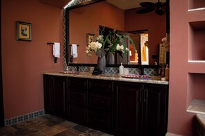 Un bagno con un vanità in legno scuro, uno specchio grande e un vaso con fiori.
