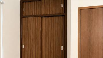 A room with a wooden wardrobe, a smaller wooden cabinet, and a wall-mounted air conditioning unit.