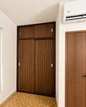 A room with a wooden wardrobe, a smaller wooden cabinet, and a wall-mounted air conditioning unit. - Casa Don Beni—Apartment 2 (Xicotepec de Juárez)
