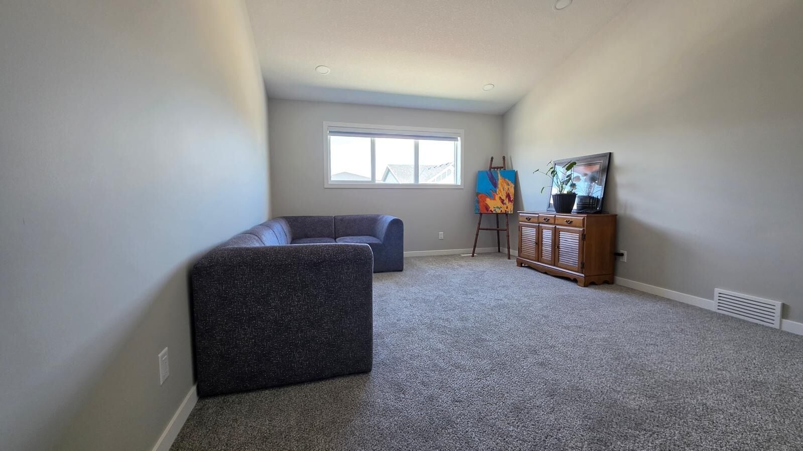 A room with a dark-colored sofa, a blue couch, a wooden cabinet, and a painting on the wall.