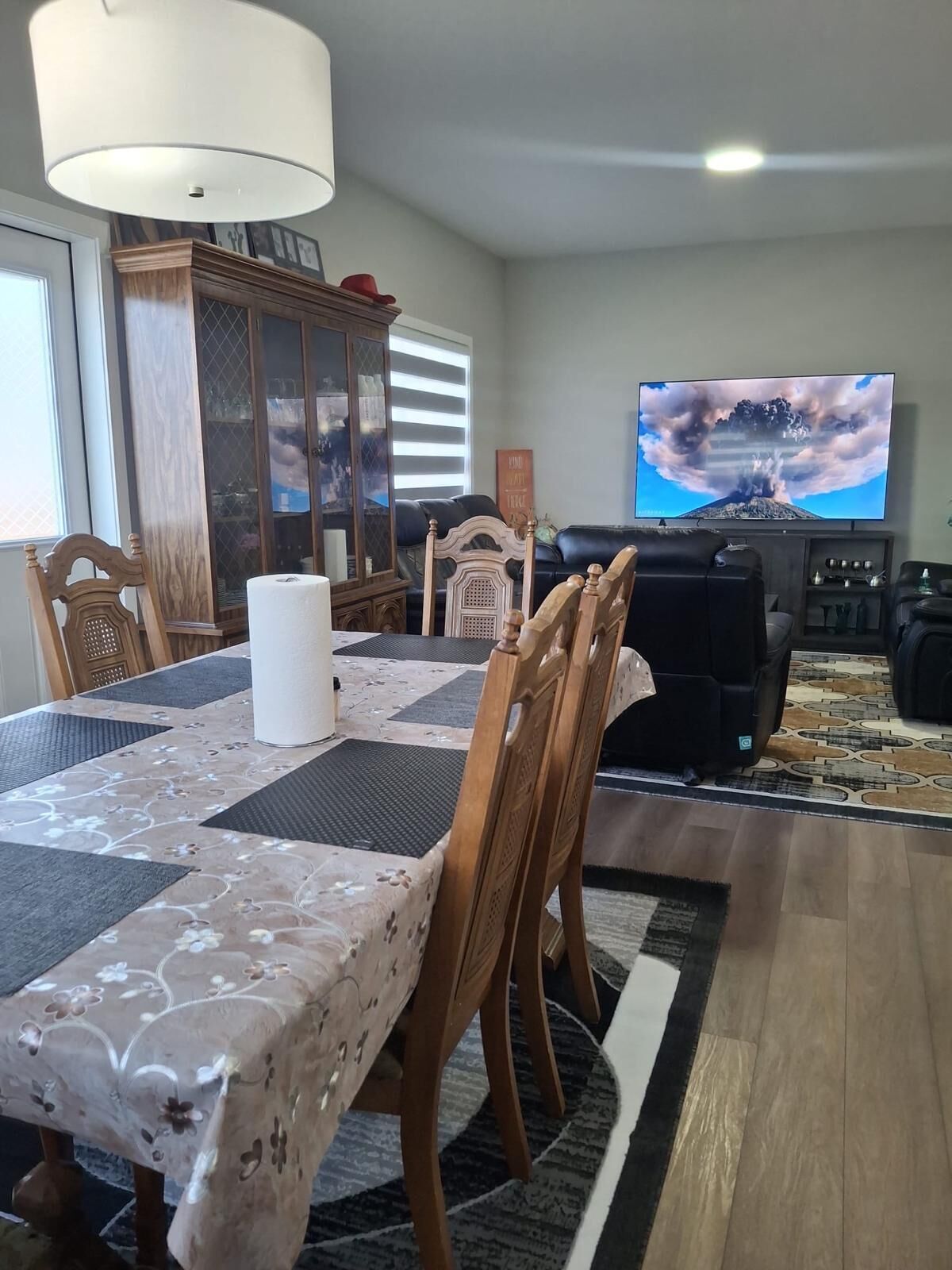 Un coin repas avec une table dressée pour quatre personnes, un téléviseur fixé au mur et un meuble avec des portes en verre.