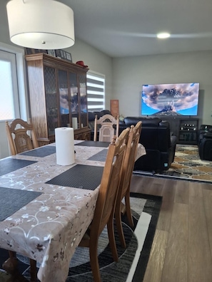 Een eethoek met een tafel voor vier personen, een aan de muur bevestigde televisie en een kast met glazen deuren.