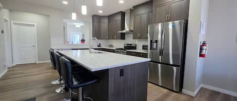 A modern kitchen with a central island, stainless steel appliances, and bar stools.