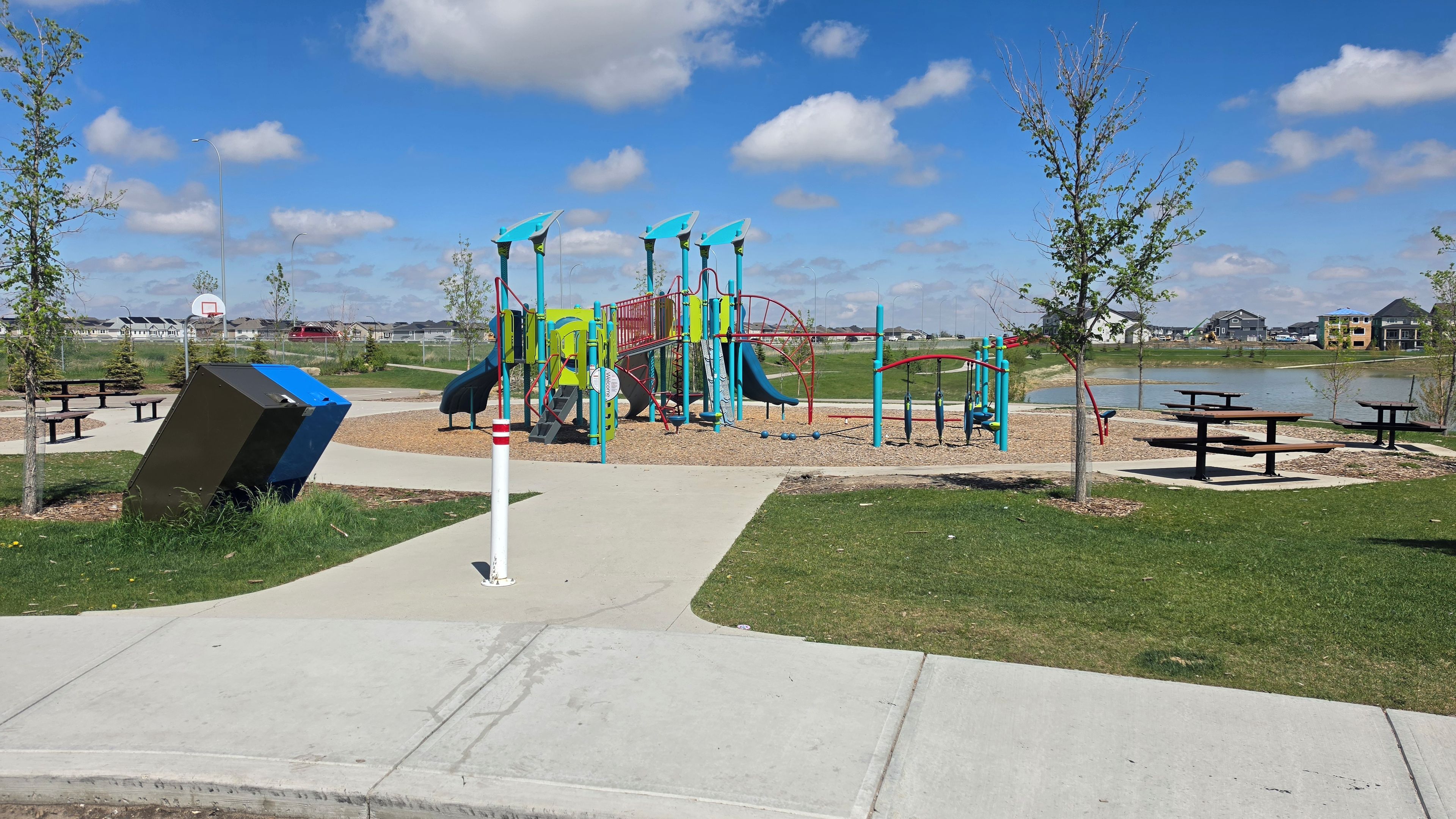 A playground with slides and swings, picnic tables, and a body of water in the background.
